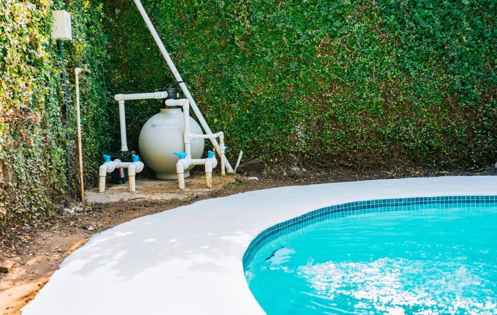 Pool pump and sand filter system installed beside a swimming pool.